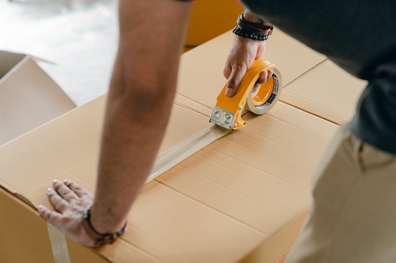 home-hero Man using packing tape to seal a cardboard box indoors. Ideal for moving or shipping concepts.